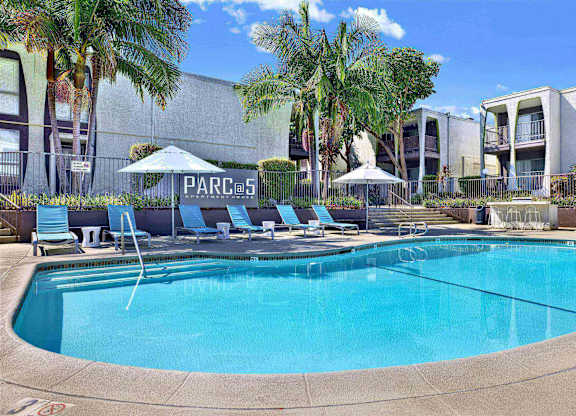 Pool area with lounge chairs and umbrellas at Parc @ 5 Apartments, Downey, 90240
