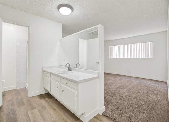 Dual vanity bathroom with carpeted bedroom view at Parc @ 5 Apartments, Downey, California