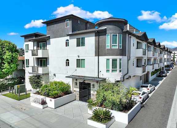 A row of modern townhouses with white and grey exteriors and green plants in front.