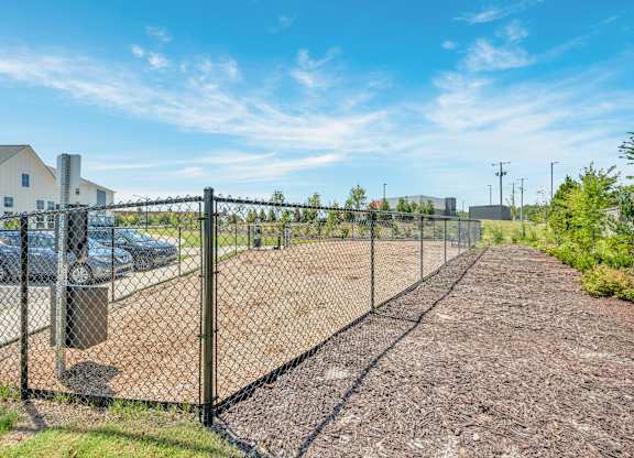 A chain link fence separates a gravel area from a grassy area.