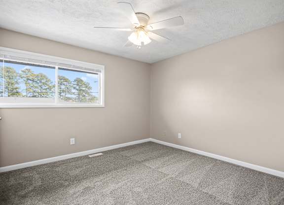 A room with a ceiling fan and a window showing trees outside.