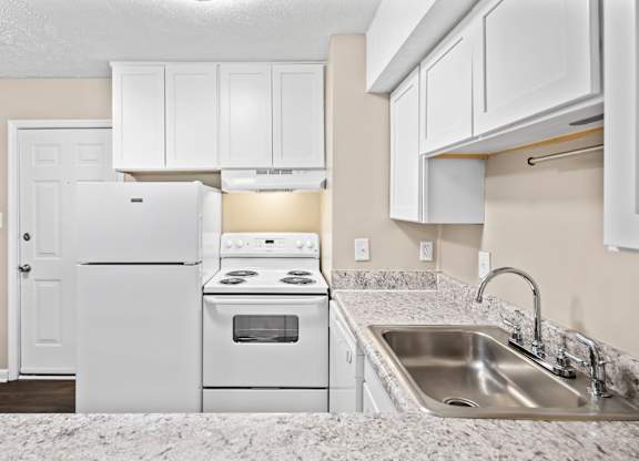 A white kitchen with a refrigerator, oven, and sink.