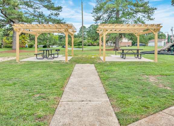 A park with a wooden pergola and picnic tables.