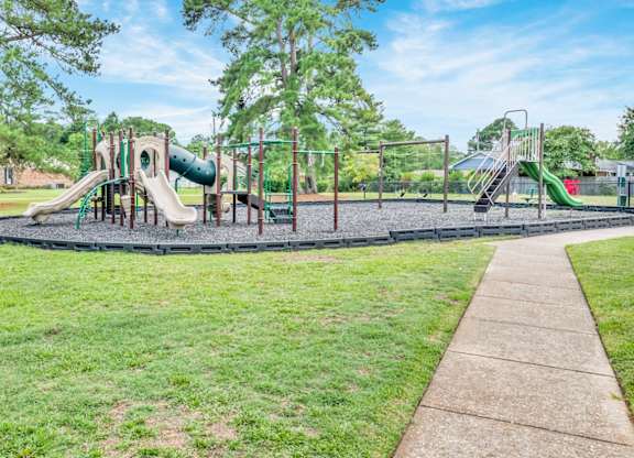 A playground with a green slide and a brown walkway.