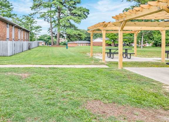 A grassy area with a wooden pergola and picnic tables.