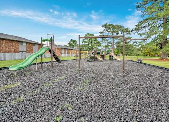A playground with a green slide and a wooden swing set.