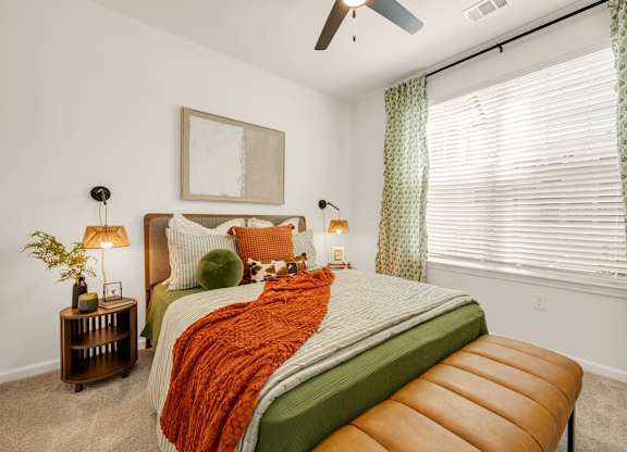 A bedroom with a bed, a bench, and a ceiling fan.