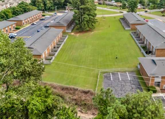 A parking lot is in front of a building with a green lawn in the middle.