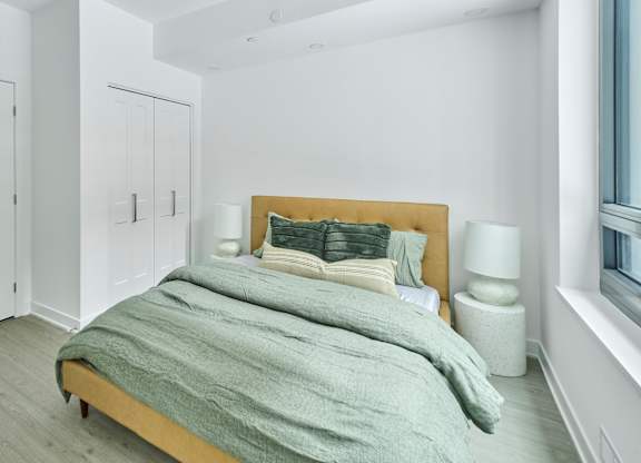 a bedroom with white walls and a bed with grey blankets and pillows