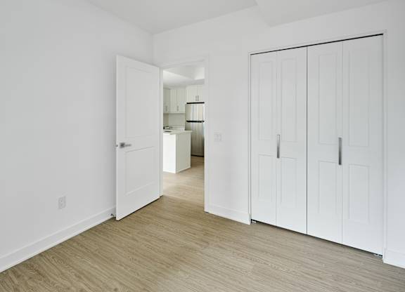 a bedroom with white walls and white closets and a wood floor