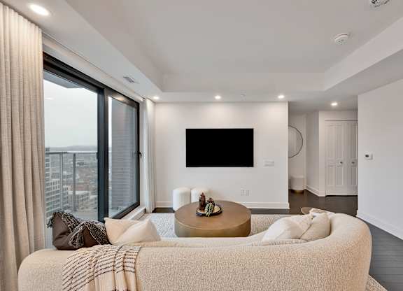 A modern living room with a large couch and a flat screen TV mounted on the wall.