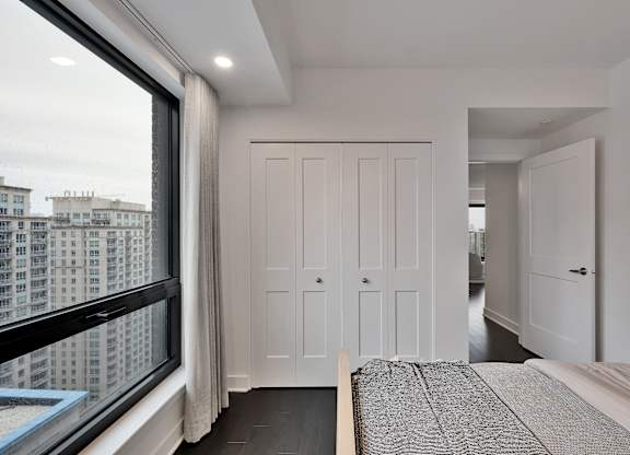 A bedroom with a large bed and a view of a cityscape through a window.