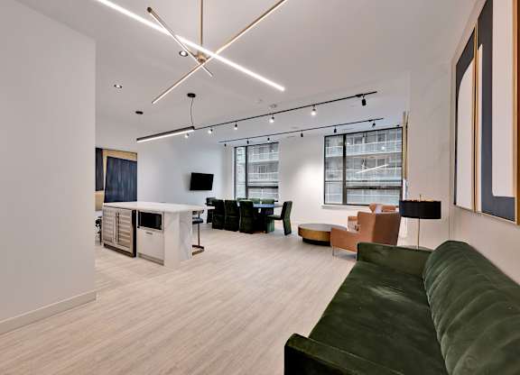 A modern living room with a green couch and a kitchen area in the background.