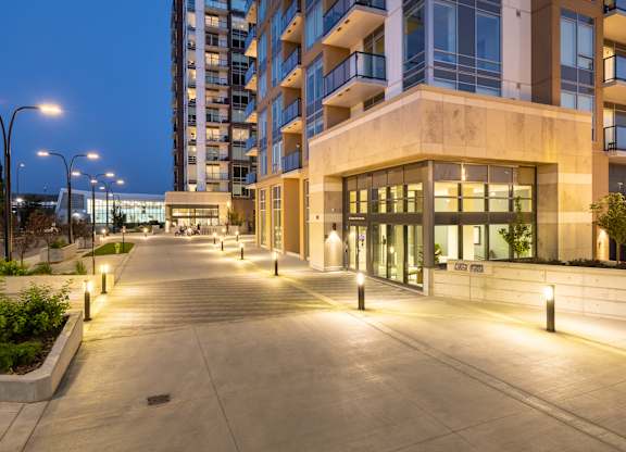 A long concrete walkway leads to a building with glass windows and doors.