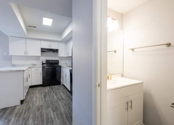 A white kitchen with a black dishwasher and a white bathroom with a white sink.