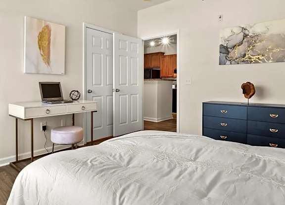 A bedroom with a bed, desk, and drawers.