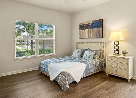 A bedroom with a bed, nightstand, and a window with a view of trees and a fence.
