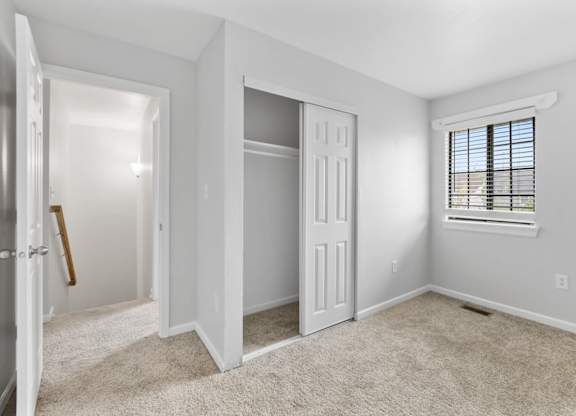 A room with a white door, a window with blinds, and a carpeted floor.