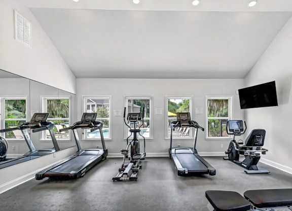 A spacious home gym with treadmills, elliptical machines, and a television.