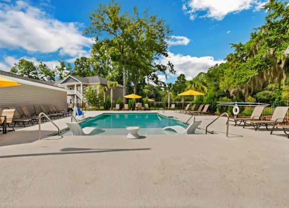 A pool surrounded by trees and chairs.