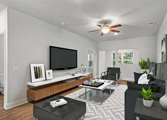 A modern living room with a flat screen TV, a coffee table, and a ceiling fan.