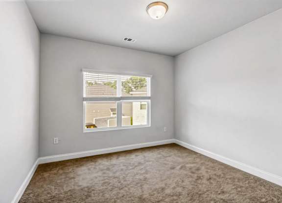 A room with a window showing a view of a house and trees.