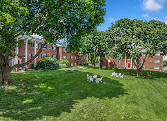 A large grassy area with trees and a row of buildings in the background.