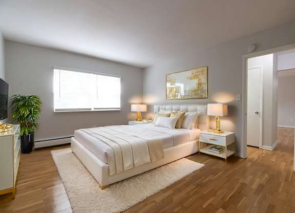 A bedroom with a large bed, a potted plant, and a painting on the wall.
