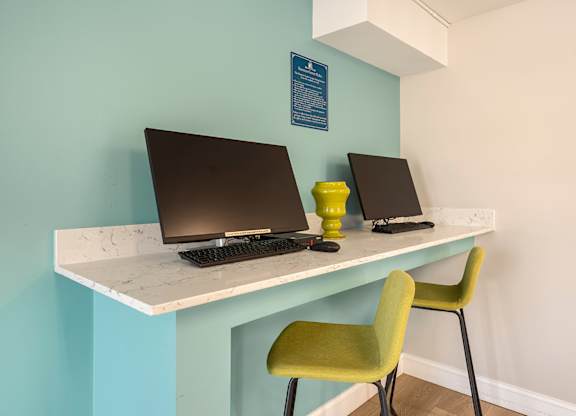 Two laptops are on a desk with a green chair.