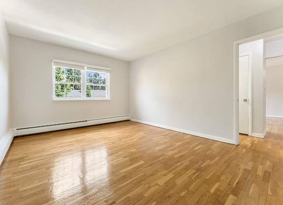 A room with wooden floors and a window showing trees outside.