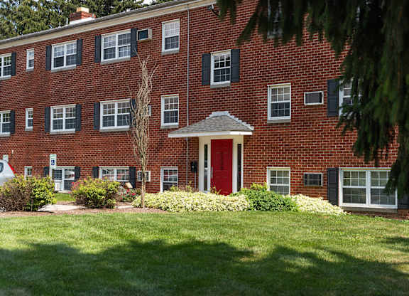 A red brick building with a red door and green bushes in front.