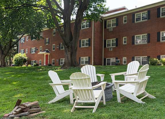 Four white chairs are placed on a lawn in front of a red brick building.