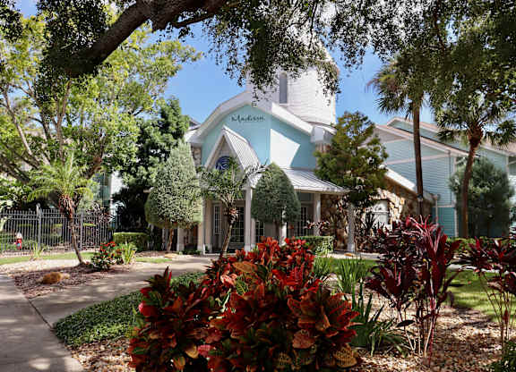 A house with a blue and white exterior is surrounded by trees and plants.