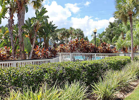 A white fence separates a grassy area from a garden with a variety of plants.