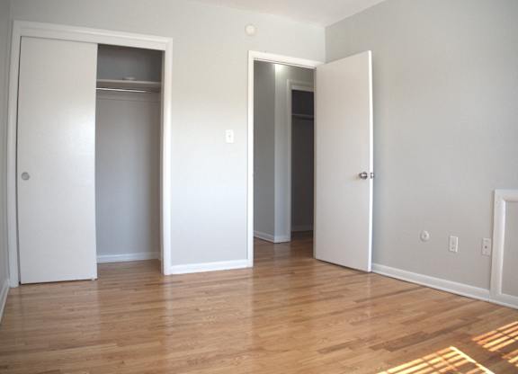 an empty living room with a wood floor and three closet doors