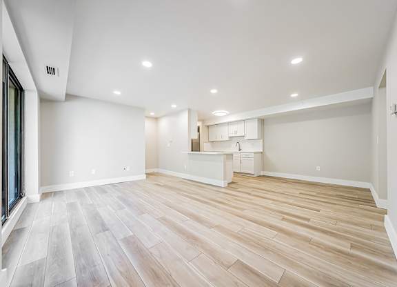 A spacious room with wooden flooring and a kitchenette in the background.