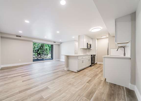 A spacious kitchen with wooden flooring and white cabinetry.