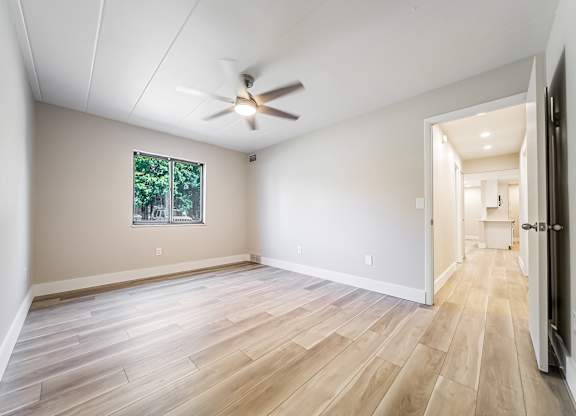 A room with a ceiling fan and a window with a view of trees.