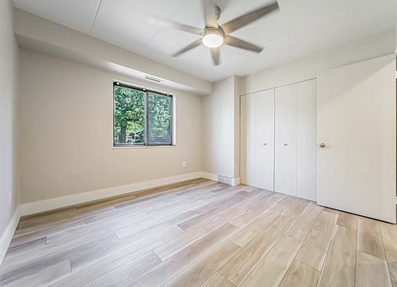 A room with a ceiling fan and a window with a view of trees.