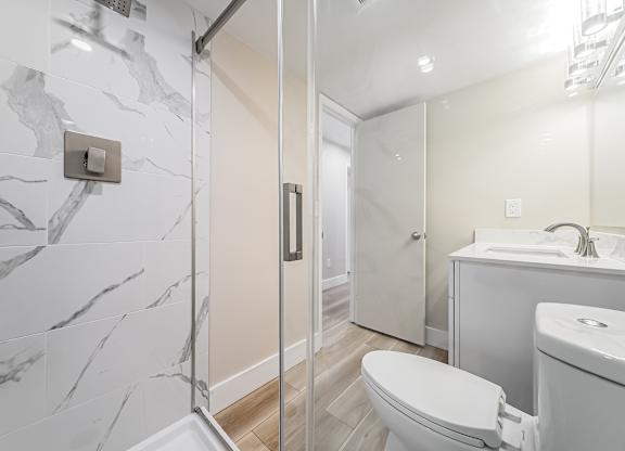 A bathroom with a marble tile shower and a white toilet.