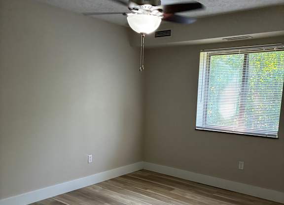 A room with a ceiling fan and a window with blinds.