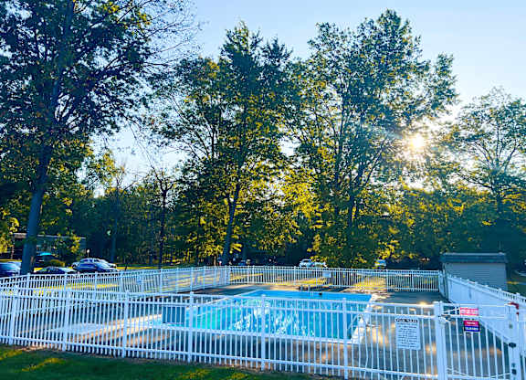 A pool surrounded by a white fence with trees in the background.