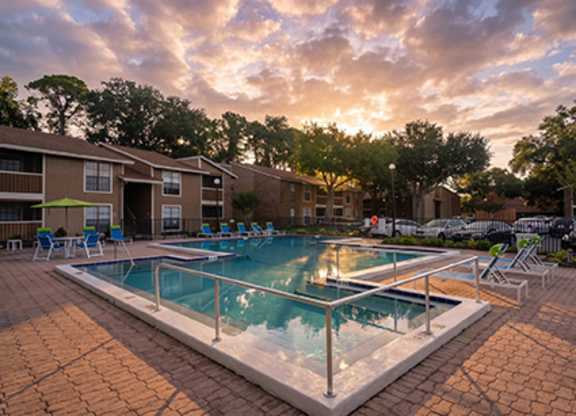 A swimming pool surrounded by a brick patio and chairs.