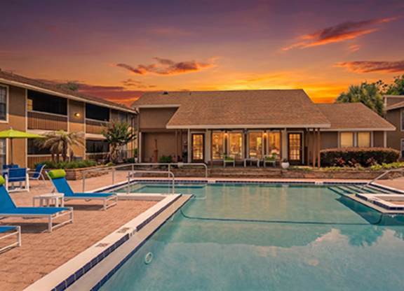 A swimming pool in front of a house with a sunset in the background.