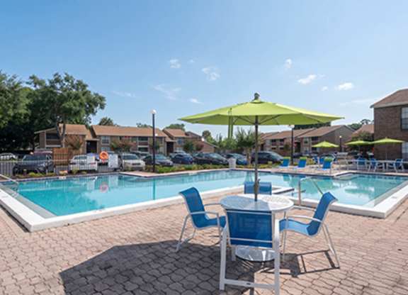A pool area with a table and chairs and a green umbrella.