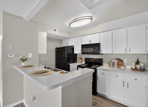 A kitchen with white cabinets and a black refrigerator.