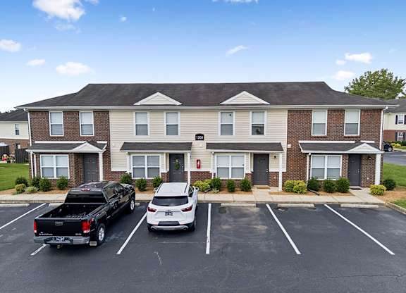 Two cars are parked in a parking lot in front of a brick apartment building.