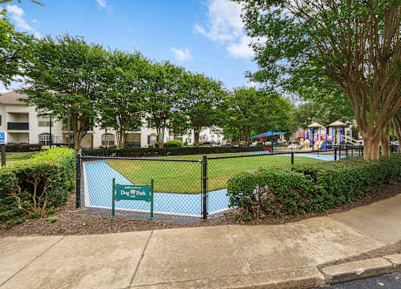 A dog park is surrounded by a black fence and has a sign that says Dog Park.
