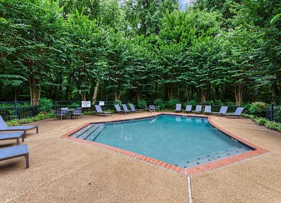 A pool surrounded by trees and lounge chairs.