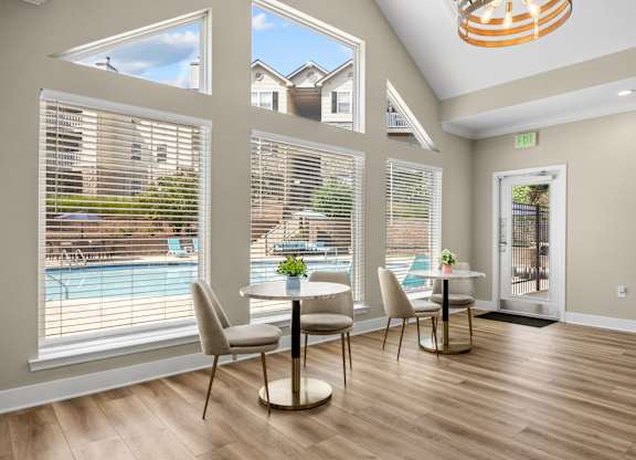 A dining room with a table and chairs and a view of a pool and houses outside the window.